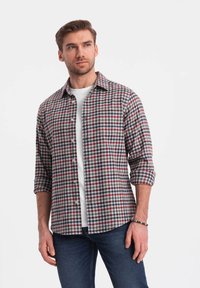 Camicia di flanella a quadri rossi, blu e bianchi con maniche lunghe, colletto button-down e taschino sul petto, indossata sopra una t-shirt bianca.
