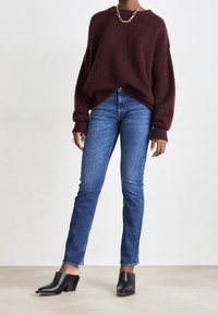 Burgundy fluffig tröja med breda ärmar, ihopparad med tajta blå jeans. Svarta mule-skor med blockklack och öppen tå.