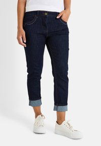 Jeans índigo oscuros con un diseño ajustado y puños enrollados. Cuenta con cinco bolsillos con costuras en contraste y un cierre de botón frontal.