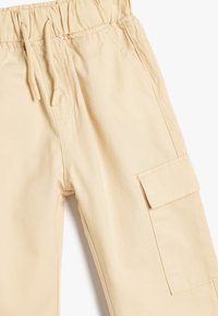Beige cargo bukser lavet af blødt stof, med elastisk talje, snørre, sidelommer og en patchlomme på benet.