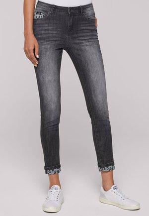 Black denim jeans with a sleek fit, featuring light gray faded areas and a leopard print accent on the cuffs. Paired with white sneakers.