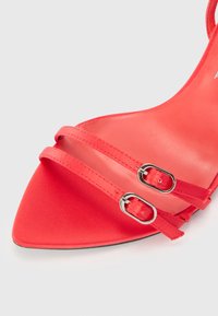 Rød satinhøyhælte sandal med spiss tå, med to slanke justerbare stropper og rektangulære sølvspenner. Glatt tekstur.