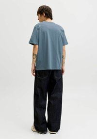 Svetlo modra bombažna majica s kratkimi rokavi in sproščenim krojem, kombinirana s temno modrimi širokimi kavbojkami in bež supergami.