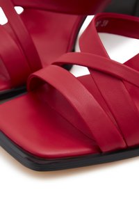 Rode leren sandalen met kruisbanden, vierkante neus en een zwarte zool. De textuur is glad met een matte afwerking.