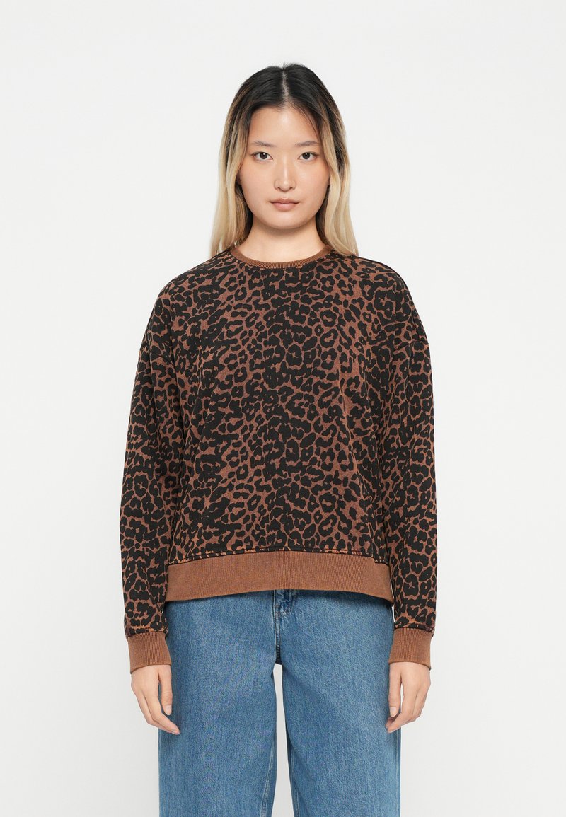 Sweater com padrão de leopardo em castanho e preto. Gola redonda, corte relaxado, punhos e bainha canelados, textura suave, combinado com jeans azuis claros, de corte solto.