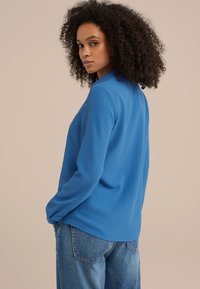 Camicia azzurra a maniche lunghe in un tessuto liscio, con una vestibilità comoda e uno spacco laterale sull'orlo, abbinata a jeans in denim azzurro chiaro.