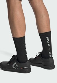 Scarpe da ginnastica nere con superfici texture e un logo, abbinate a calze nere a coste con scritte bianche "FIVE TEN."