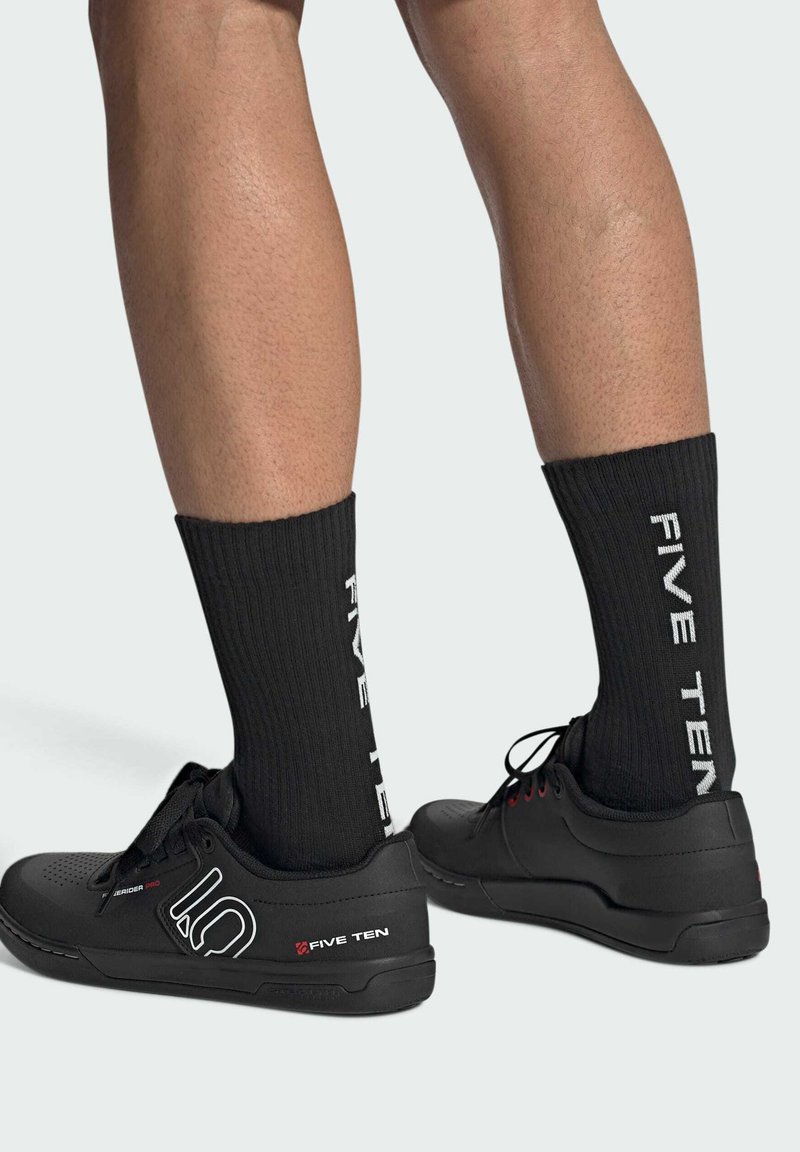 Scarpe da ginnastica nere con superfici texture e un logo, abbinate a calze nere a coste con scritte bianche "FIVE TEN."