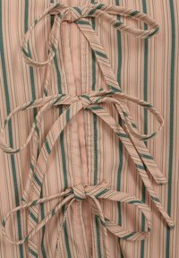 Tissu rose pâle avec des rayures verticales vert foncé et blanches. Comprend des fermetures à rubans noués et une finition lisse et texturée.