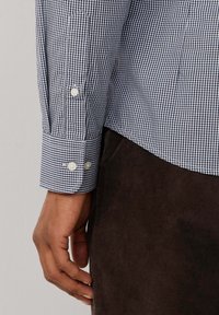 Camisa de cuadros vichy azul y blanca con puños abotonados y un corte ajustado, complementada con pantalones de pana marrones.