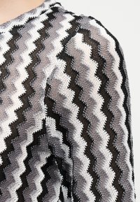 Κοντινό πλάνο υφάσματος πλεκτού σε ζιγκ-ζαγκ με μαύρο, λευκό και γκρι χρώμα, με υφή και ανοιχτό πλέξιμο σε ρούχο.