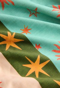 Tissu avec un motif d’étoiles orange et jaunes sur des parties vertes et bleu clair, montrant la texture et les plis.