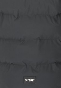 Svart puffjacka med horisontella quiltade sektioner och en slät textur. Har en rektangulär logotypapplikation märkt "SLOPE."