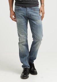 Jeans de mezclilla azul claro con un degradado gradual, corte recto, cinco bolsillos y sutiles detalles de costura, combinados con zapatos negros de cordones.