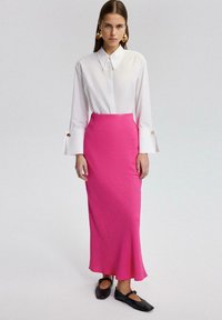 Valkoinen kauluspaita pitkillä hihoilla ja nappidetaililla yhdistettynä slim fit vaaleanpunaiseen tekstuurimaksi-hameeseen ja mustiin tasapohjaisiin kenkiin.