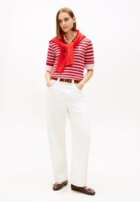 Punaste ja valgete triipudega lühikeste varrukatega särk, kombineeritud laia valgete pükstega ning pruuni värvi baleriinikingadega. Õlgade ümber on mähitud oranžast lõngast sall.