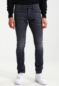 Smal passform mörkblå denimjeans med subtil blekning, fem fickor och dragkedja, kombinerat med vita sneakers.