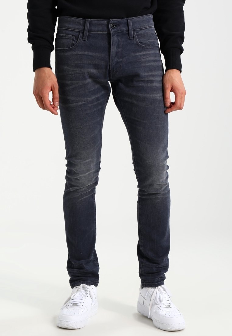Smal passform mörkblå denimjeans med subtil blekning, fem fickor och dragkedja, kombinerat med vita sneakers.
