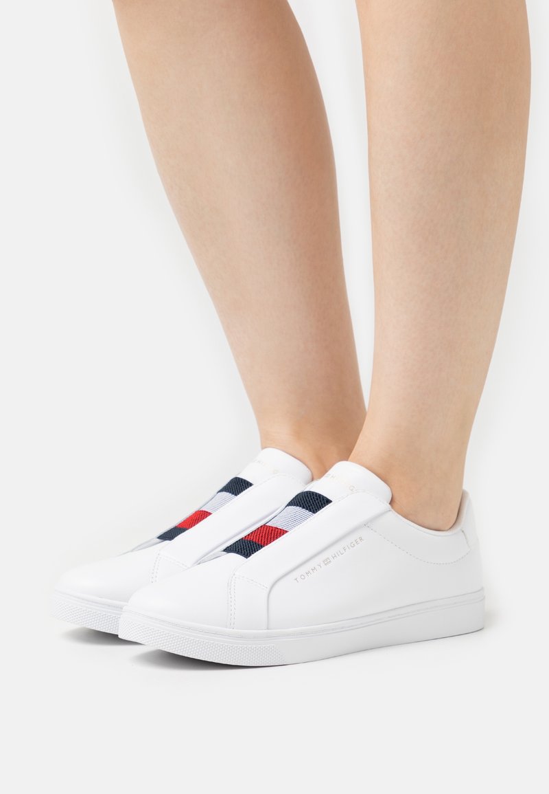 Weiße Slip-On-Sneaker mit elastischen Bändern in marineblau, rot und weißen Streifen. Glattes synthetisches Material mit einer strukturierten Gummisohle.