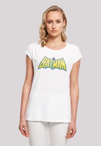 White cotton t-shirt with rolled sleeves, featuring a large yellow and blue "BATMAN" graphic on the front. Smooth texture, relaxed fit.