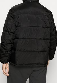 Černá péřová bunda s prošívaným designem, vodorovnými švy, stojatým límcem a hladkou, lesklou texturou.