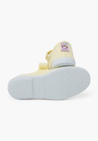 Scarpe di tela gialle con cinturino in velcro, suola in gomma bianca e suola testurizzata. Presentano un'etichetta colorata di una scimmia sul tallone. Taglia 28.