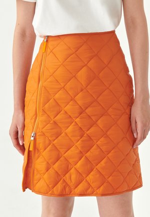 Jupe matelassée orange avec une fermeture éclair sur le côté, motif rectangulaire et texture lisse. Association avec un haut blanc visible.