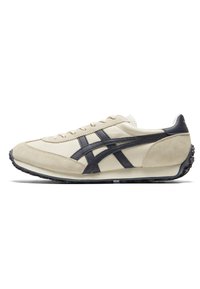 Scarpa da ginnastica beige realizzata in pelle e suede, con strisce blu scuro e suola in gomma nera texturizzata. Design minimalista con chiusura con lacci.