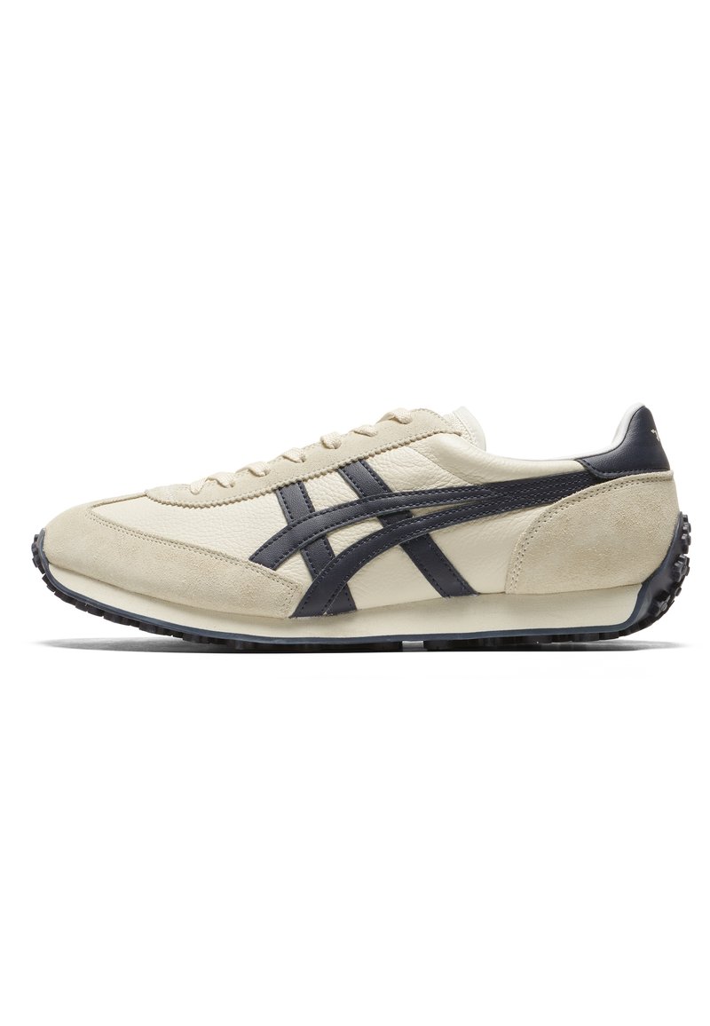 Scarpa da ginnastica beige realizzata in pelle e suede, con strisce blu scuro e suola in gomma nera texturizzata. Design minimalista con chiusura con lacci.