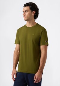 Olijfgroene katoenen T-shirt met een ronde hals, korte mouwen en een klein geborduurd logo op de borst en mouw. Soepele textuur.