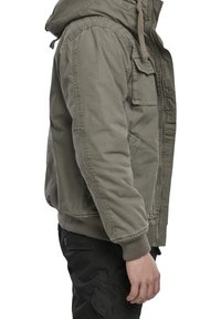Zielona bawełniana kurtka z kapturem, wyposażona w przednie kieszenie, ściągacze na mankietach i zapięcie na zamek. Materiał ma teksturowany, casualowy wygląd.
