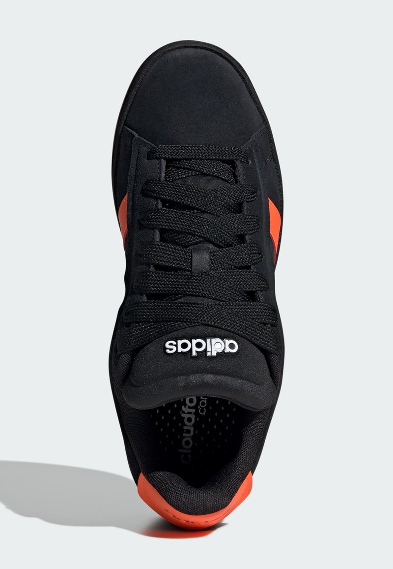 Chaussure de sport noire avec des accents orange, dotée d'une tige en suède texturé, d'un laçage et d'un logo sur la languette. Semelle en caoutchouc.