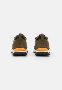 Grønne ruskindssneakers med sorte detaljer, med en orange hælclip og hvid mellemsål. Tekstureret ydersål med synlige slidmønstre.