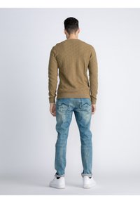 Bruine gebreide trui met lange mouwen, gecombineerd met lichtblauwe vervaagde jeans en witte sportschoenen, bekeken vanuit de achterkant.