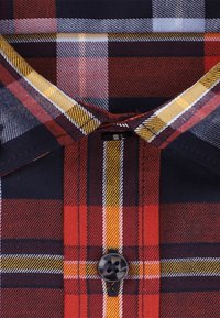 Koszula w kratę z kołnierzykiem w czerwono-granatowo-żółto-białym wzorze, z czarnym guzikiem na cztery otwory zapiętym u kołnierza.