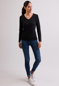 Maglione nero a maniche lunghe con scollo a V abbinato a jeans fitted blu e sneakers bianche. Texture morbida con un design semplice e minimalista.