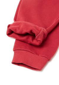 Červené tepláky s žebrovanými manžetami, které mají na vnitřním okraji měkkou fleecovou podšívku. Látka má hladký povrch a jednotnou barvu.