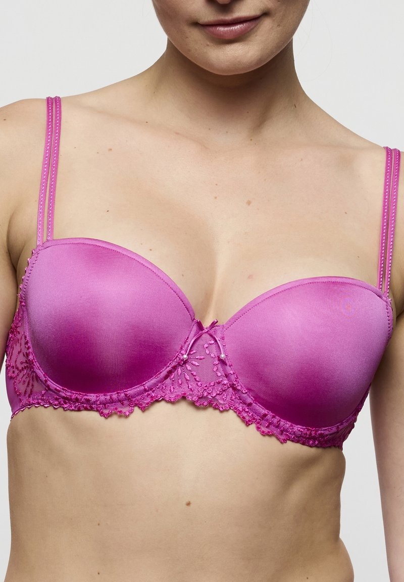 Soutien-gorge en satin rose avec bonnets rembourrés, orné de détails en dentelle en bas et de fines bretelles réglables. Présente un nœud décoratif au centre.