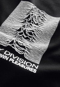 Black T-shirt featuring a white design with wavy lines resembling mountain peaks and text that reads "JOY DIVISION – UNKNOWN PLEASURES."