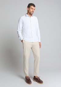 Witte lange mouwen blouse met een knoopsluiting aan de voorkant, gecombineerd met beige broeken en bruine schoenen met roze veters en een gestructureerde zool.