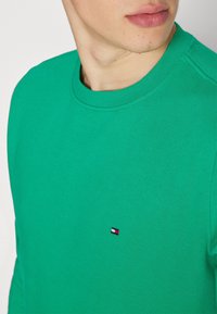 Felpa verde con girocollo in cotone, dotata di un piccolo logo ricamato sul petto. Il tessuto presenta una texture liscia e un colore uniforme.