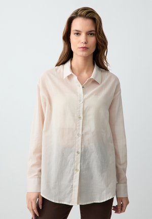 Blusa lunga a maniche in beige chiaro in tessuto trasparente, con chiusura a bottoni frontale, colletto classico e orlo dritto.
