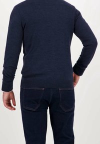 Suéter azul marino de manga larga con tejido texturizado, con dobladillo y puños acanalados, combinado con jeans oscuros visibles a la altura de la cintura.