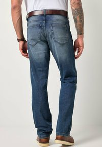 Vaqueros de mezclilla azul oscuro con corte de pierna recta, bolsillos traseros visibles, ligero desgaste y un cinturón de cuero marrón. Se llevan zapatos marrones.