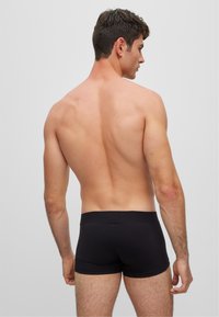 Boxers de algodón negros con un ajuste ceñido, textura suave y cinturilla elástica, exhibidos en un modelo masculino visto desde atrás.