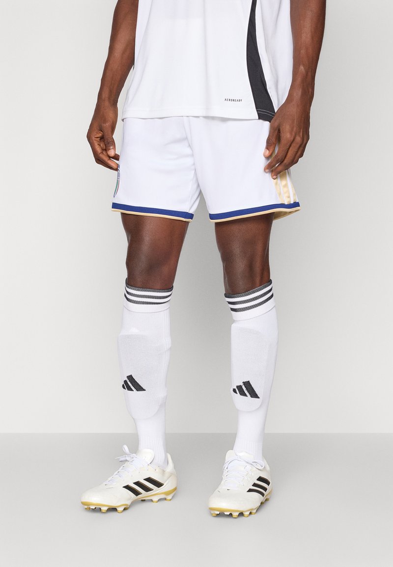 White soccer shorts with gold and blue trim, paired with white socks featuring black stripes and logo, and white cleats with black accents.