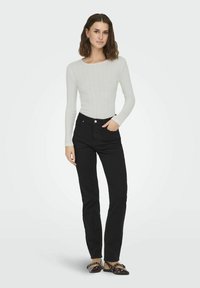 White ribbed long-sleeve top with a round neckline, paired with high-waisted black jeans and flat burgundy shoes with silver hardware.
