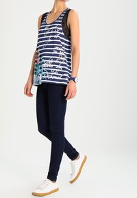 Marinblå randig linne med blommönster och vit text, med spetsdetaljer vid axlarna. Matchas med mörka jeans och vita sneakers.