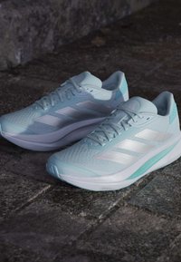 Hellblaue Sportschuhe mit einem strukturierten Mesh-Obermaterial, weißen Streifen und einer gepolsterten Sohle. Verfügt über ein strukturiertes Schnürdesign.