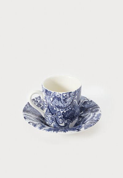 Tazza e piattino in porcellana, con intricati motivi floreali blu e spirali su sfondo bianco, dotati di un manico curvo sulla tazza.